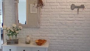 A white console table with a mirror, a vase with flowers, and a small plant. - Large, cozy vacation home with garden between St. Peter-Ording & Büsum (Wesselburen)