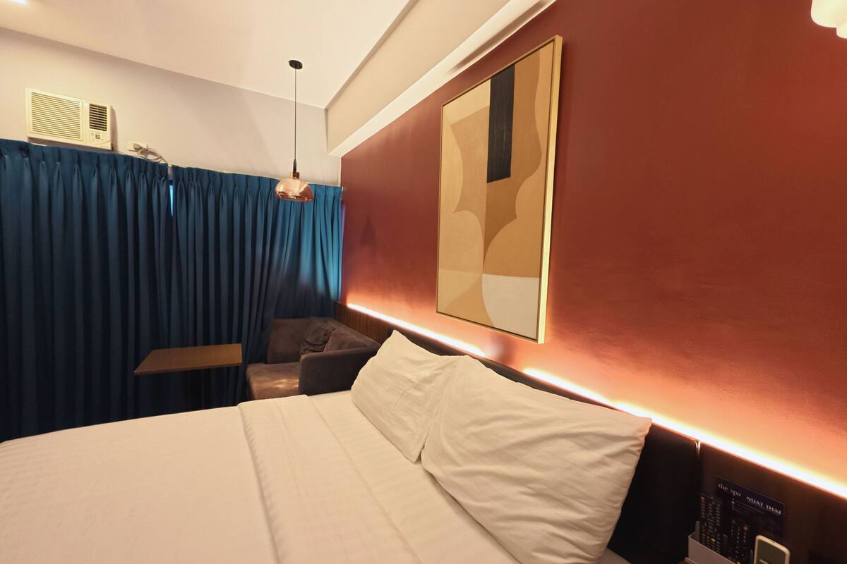 Habitación de hotel con una cama grande, un escritorio, una silla, un televisor montado en la pared y un ventilador de techo.