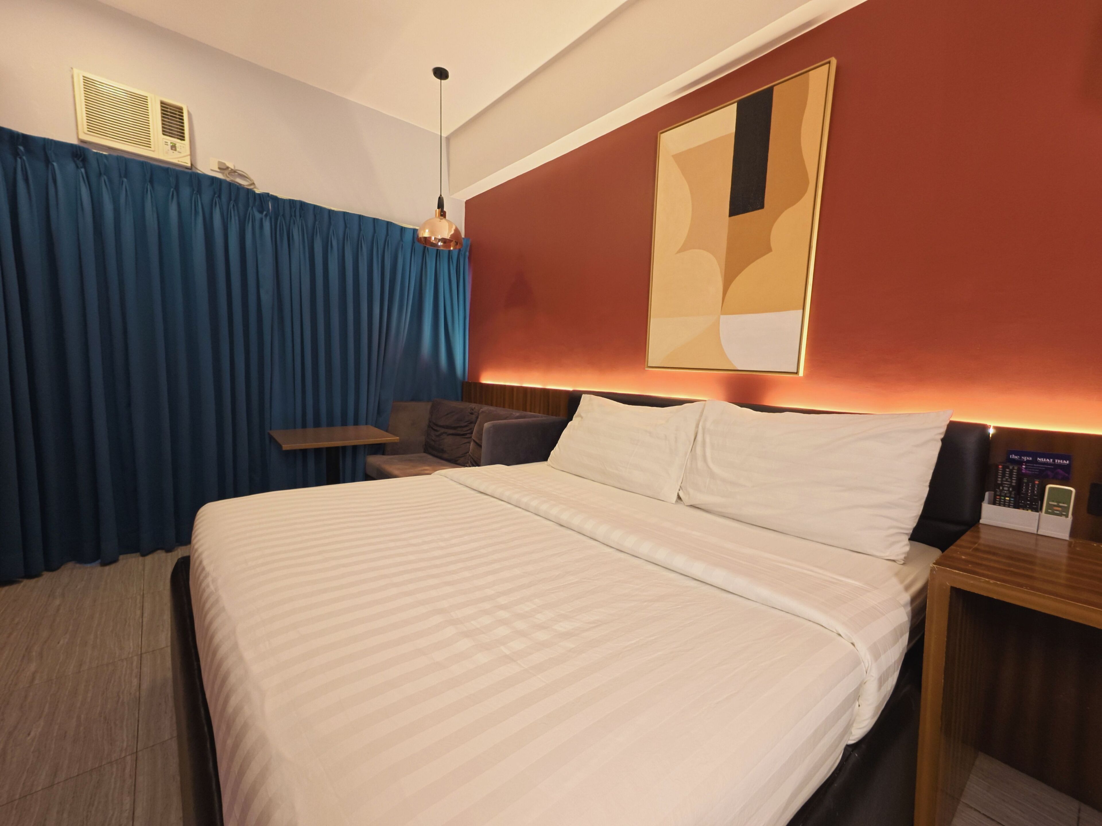 Une chambre d’hôtel avec un grand lit, une petite table, un canapé et un téléviseur fixé au mur.