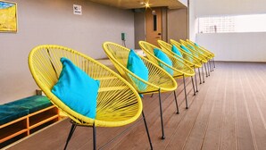 Une rangée de chaises en osier jaune, dotées de coussins bleus, se trouve dans une pièce dont le sol est en bois et où un tableau est accroché au mur.