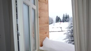 Ein Fenster mit einer Holzbank, Blick auf eine verschneite Landschaft mit Bäumen und einem klaren Himmel.