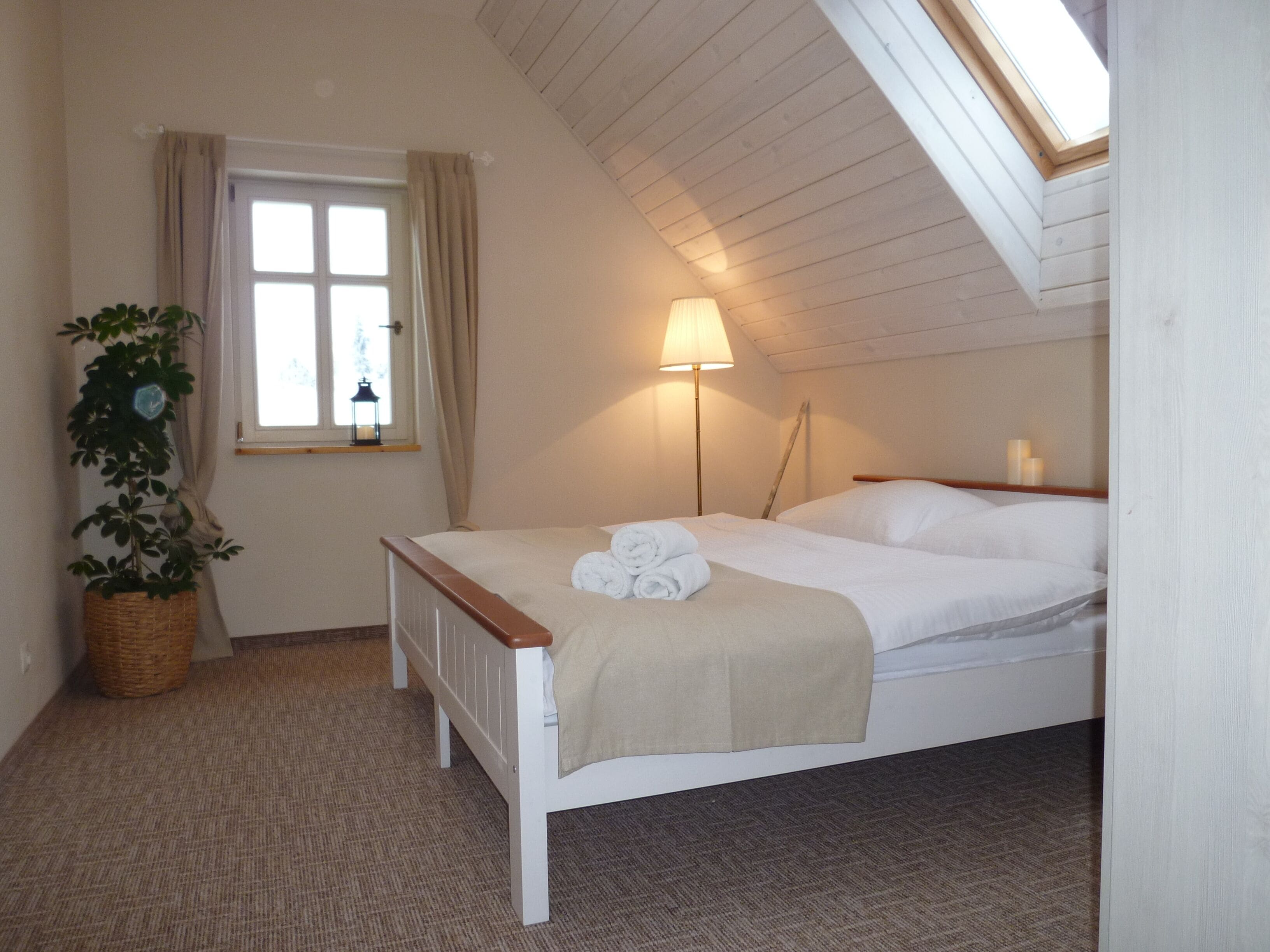 A bedroom with a bed, a lamp, a window with curtains, and a plant.