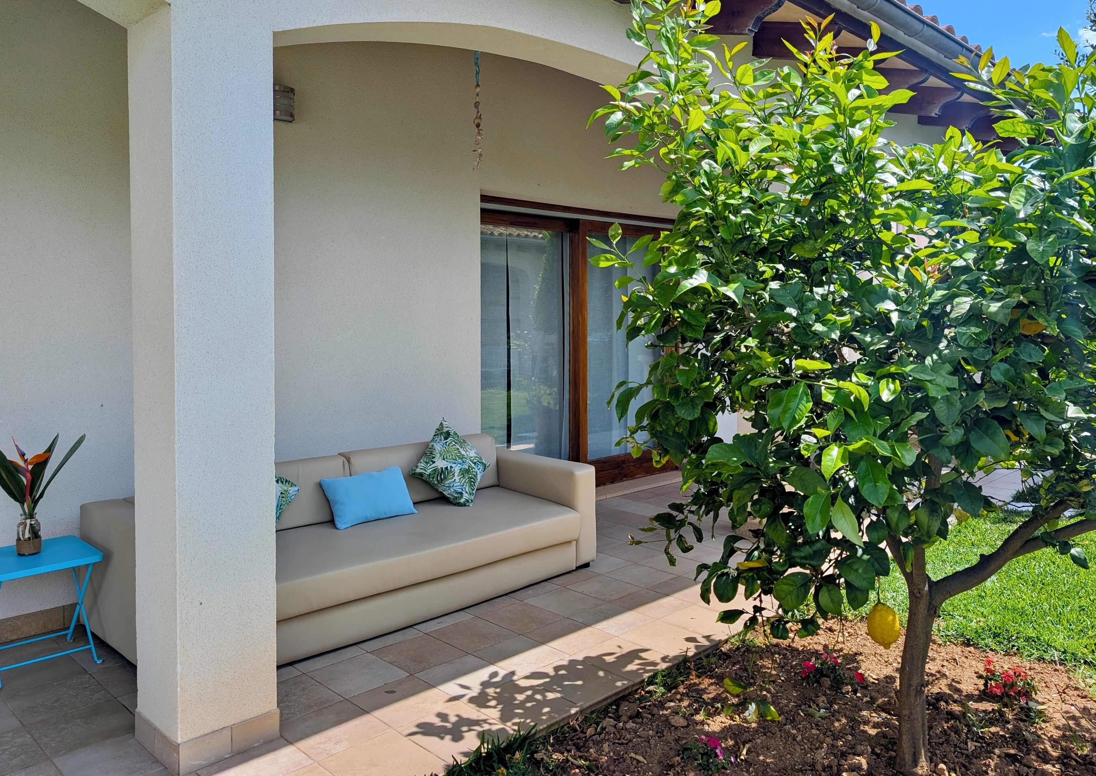 A covered outdoor seating area with a sofa, a small table, and a potted plant.
