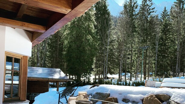 A wooden deck with a view of snow-covered ground and trees.
