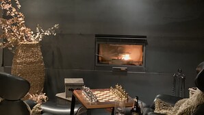 A modern living room with a fireplace, two leather chairs, a chess table, and a decorative vase.