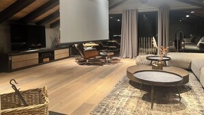 A modern living room with a flat-screen TV, comfortable seating, a coffee table, and a large window with curtains.