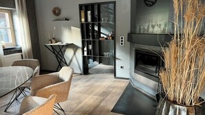 A modern living room with a fireplace, a dining area with chairs, and a glass cabinet with bottles.