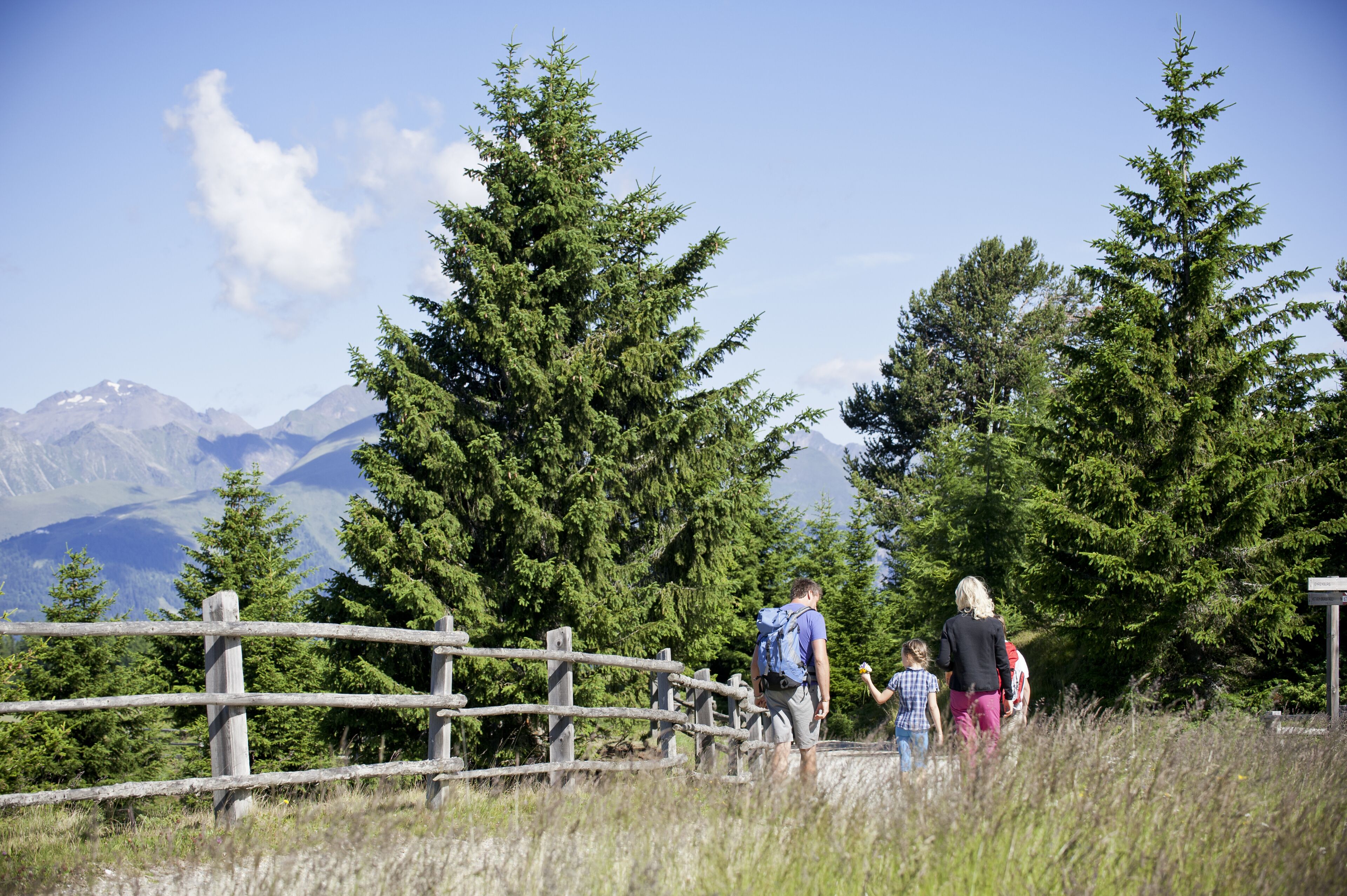 Un grupo de personas caminando cerca de una valla de madera con un paisaje montañoso al fondo.