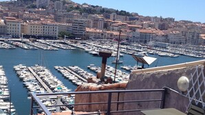 A marina with numerous boats docked, a cityscape in the background, and a wooden deck with a table and chairs. - Vieux Port to Notre Dame de la Garde Triplex 70 m2 terrace (Marseille)