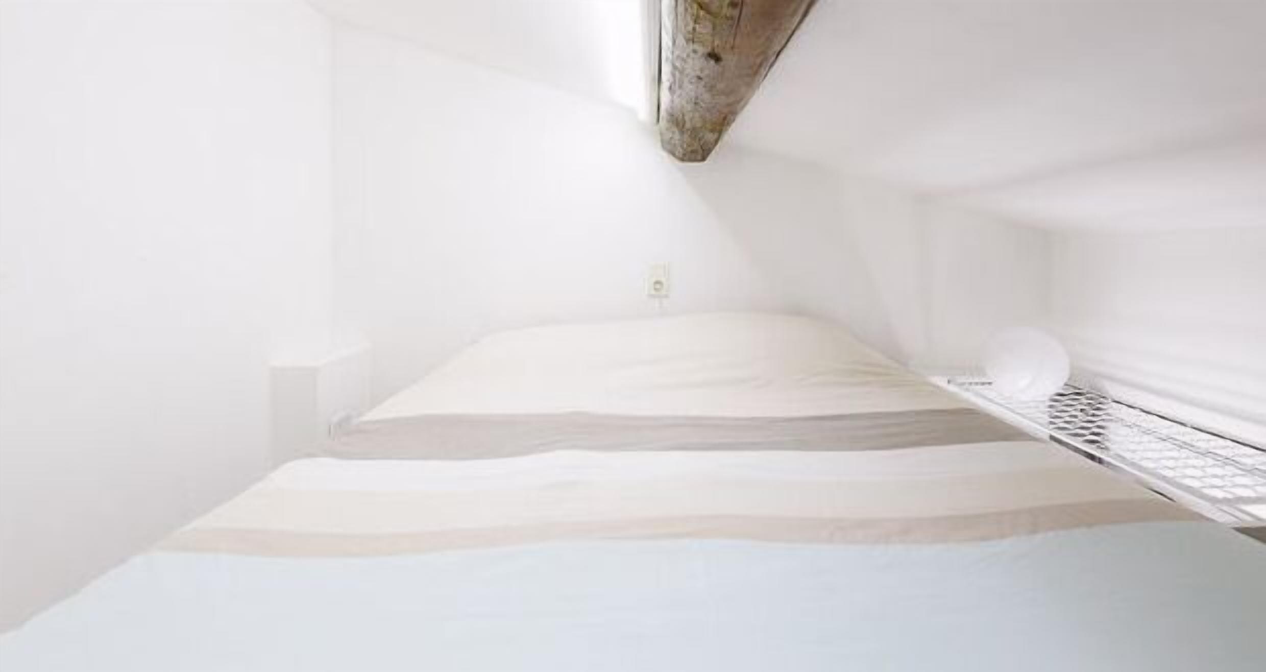 Una habitación minimalista con una cama, una mesita de noche pequeña y un estante en la pared.