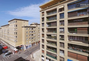 Um edifício de vários andares com varandas, uma rua para pedestres na frente e um céu claro.