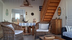 Een gezellige woonkamer met rieten meubels, een eethoek met een gestreepte tafelkleed en een houten trap.