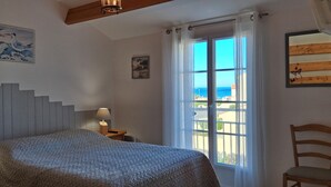 Een slaapkamer met een bed, twee nachtkastjes met lampen, een houten stoel, een groot raam met gordijnen en kunstwerken aan de muren.