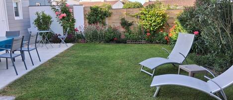 A backyard with a well-maintained lawn, two lounge chairs, and a small table.