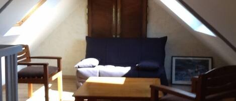 A cozy attic bedroom with a sloped ceiling, a wooden bed, a small table, and two chairs.