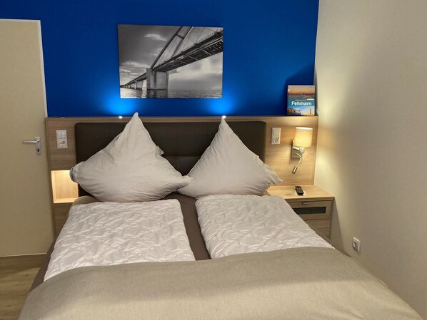 Une chambre d’hôtel avec un lit, deux oreillers blancs, une table de chevet avec une lampe et un tableau représentant un pont, accroché au mur.
