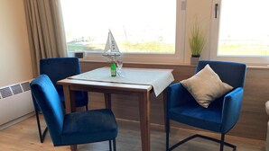 A room with a table, two blue chairs, a small sailboat model, a bottle, and a glass on the table.
