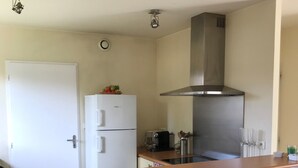 A compact kitchen with a white refrigerator, a stainless steel range hood, a wooden countertop, and two foldable chairs.