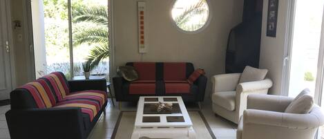 A living room with a black sofa, a red and black sofa, a white armchair, and a white coffee table. There is a large window with a view of palm trees.
