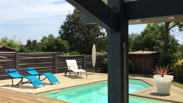 A wooden deck with a pool, blue lounge chairs, and a potted plant.