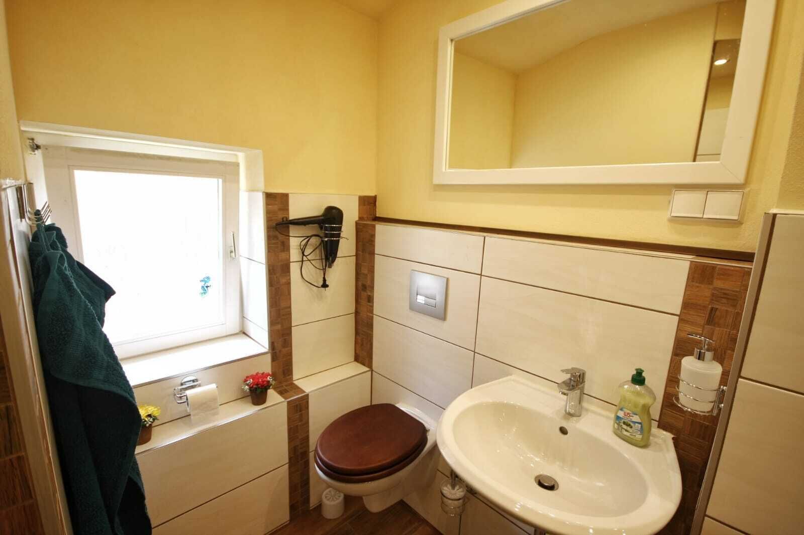 A compact bathroom with a window, a sink, a toilet, and a hairdryer mounted on the wall.