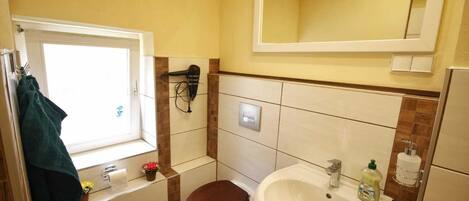 A compact bathroom with a window, a sink, a toilet, and a hairdryer mounted on the wall.