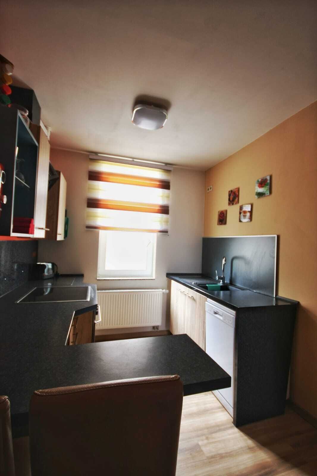 Eine kompakte Küche mit schwarzem Arbeitsplatz, einem integrierten Geschirrspüler und einem Fenster mit gestreifter Vorhang.