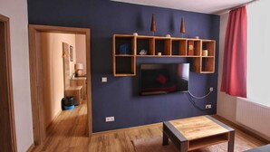 A living room with a TV mounted on a dark wall, wooden shelves above it, and a coffee table in the center. - Vacation apartment for 4 max. 5 persons in Arnstadt. Wallbox 0.59 KW (Arnstadt)