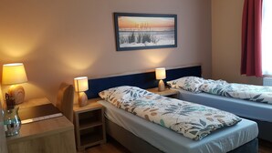 A hotel room with two beds, wooden nightstands, lamps, a small table with a vase, and a framed picture on the wall. - Vacation apartment for 4 max. 5 persons in Arnstadt. Wallbox 0.59 KW (Arnstadt)