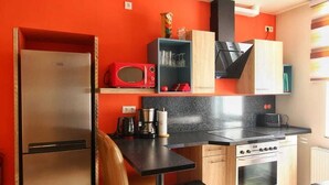 A compact kitchen with a refrigerator, microwave, stove, and a small dining area. - Vacation apartment for 4 max. 5 persons in Arnstadt. Wallbox 0.59 KW (Arnstadt)