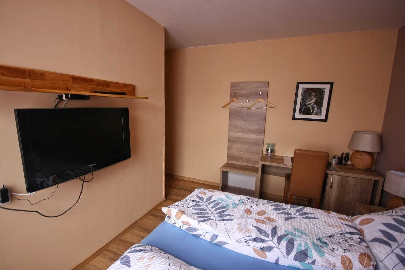 Habitación de hotel con cama, escritorio, silla, televisor montado en la pared y un cuadro enmarcado.