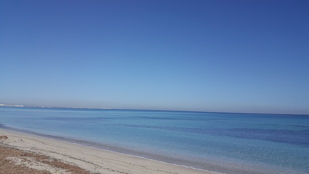 Une plage à l’eau d’un bleu limpide et au rivage sablonneux.