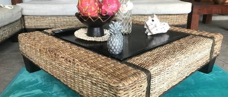 Una mesa de centro de mimbre con tapa negra, una botella decorativa y un frutero.