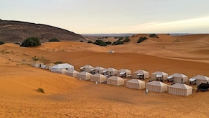 Eine Wüstenlandschaft mit mehreren in einer Reihe angeordneten Zelten, die an einen Karawanenplatz oder Campingplatz erinnern.