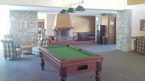 Una mesa de billar en una habitación con paredes de piedra, una chimenea y vigas de madera en el techo.