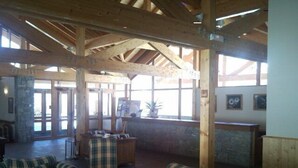 Un lobby amplio con techos altos y vigas de madera a la vista, que incluye sofás de estampado escocés y un pilar de piedra.
