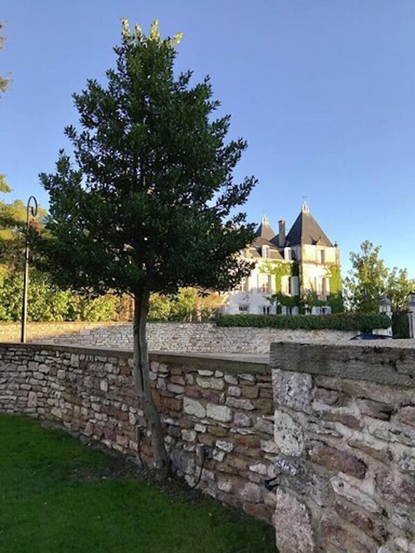 Mur de pedra amb un arbre davant d'un edifici de diverses xemeneies.