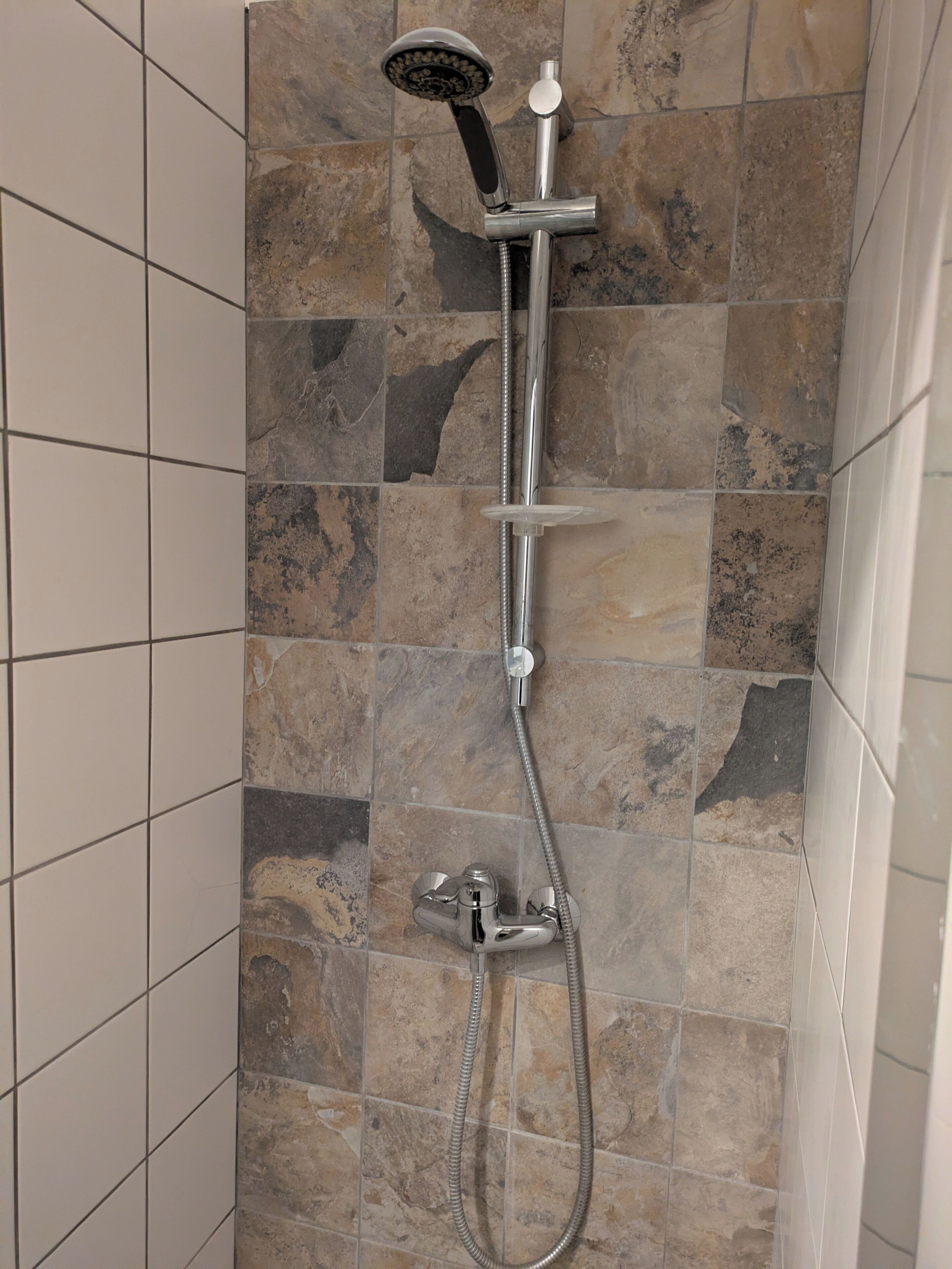 En dusch med ett duschmunstycke som kan hållas i handen och en väggmonterad blandare.