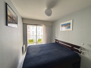 Ein Hotelzimmer mit Bett, Fenster mit Blick auf Gebäude, Deckenleuchte und einem gerahmten Bild an der Wand.