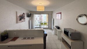 Une cuisine moderne avec un coin repas, un téléviseur fixé au mur et une vue sur l’extérieur.