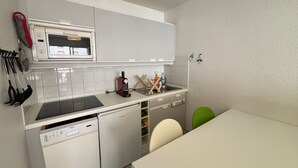 Une cuisine compacte équipée d’un lave-vaisselle, d’un four à micro-ondes et d’un évier. Des ustensiles sont accrochés au mur et une chaise verte se trouve près de la table.