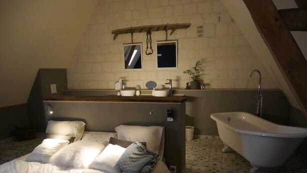 Un dormitorio con cama, un baño con bañera y una ventana pequeña.