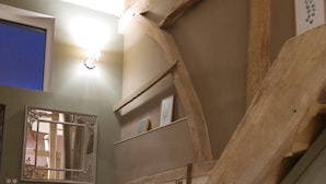 Una escalera con vigas de madera, un sofá con cojines, un espejo en la pared y un cuadro enmarcado.