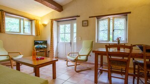 A cozy living room with a wooden table, chairs, a television, and a door leading outside. - Le Jas, charming Mas in Provence with shared pool, nature, calm, space (Flayosc)