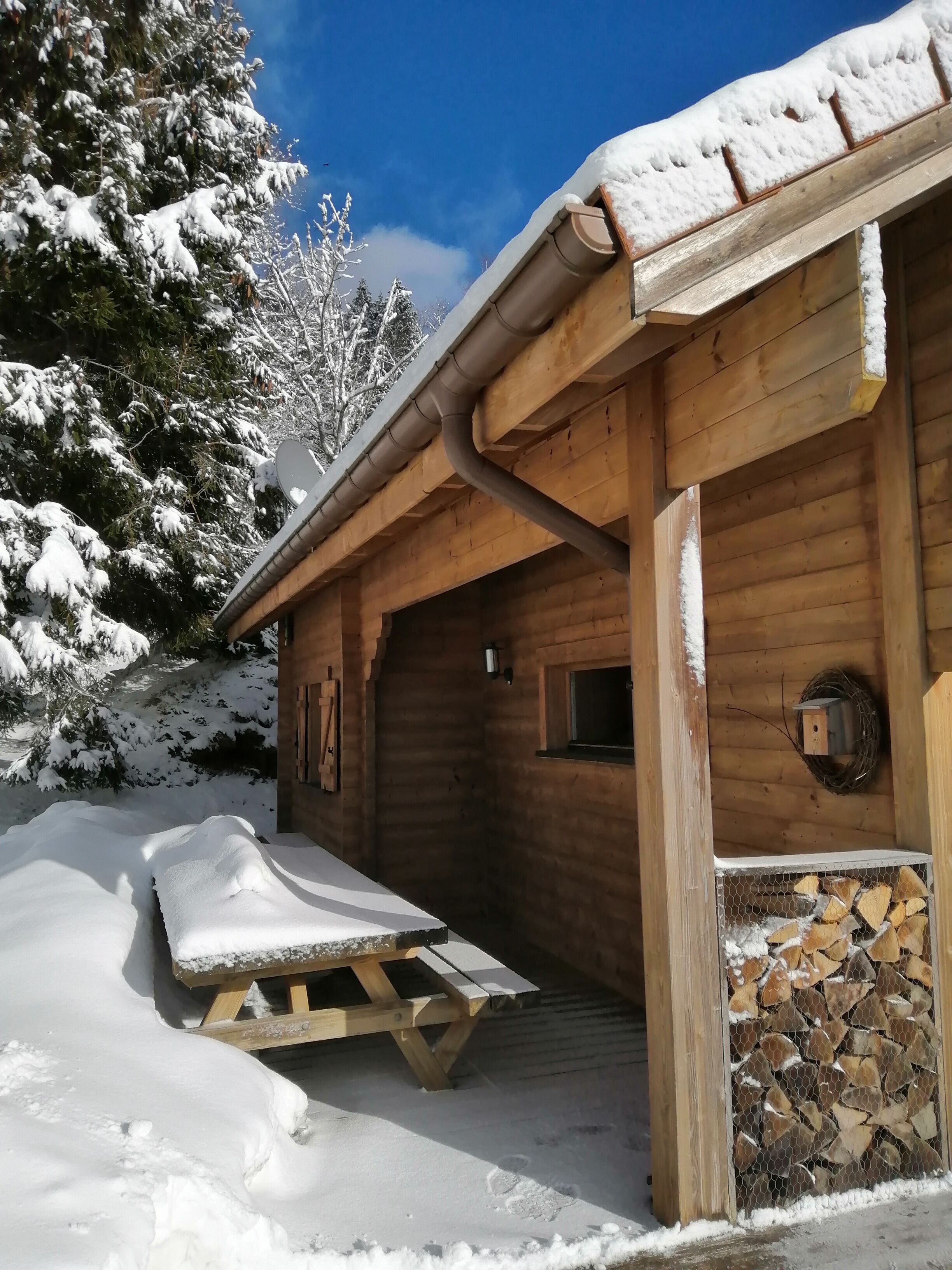 Uma cabana de madeira com telhado coberto de neve, um deque de madeira e uma chaminé.
