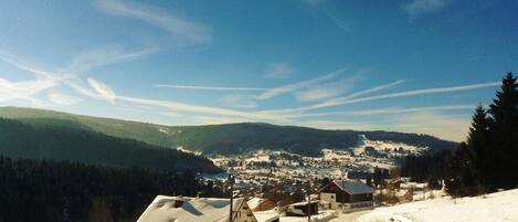 A snow-covered village with houses and a church, surrounded by mountains and a clear sky.
