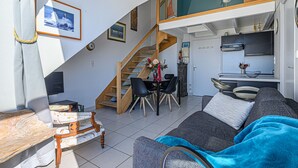A compact living space with a staircase leading to a loft, a dining area, and a kitchenette. - Seaview ! Bright veranda apartment at the foot of the beach  (Clohars-Carnoët)