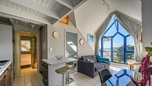 A modern kitchen with a central island, a dining area with a glass table, and a large window offering a view. - Seaview ! Bright veranda apartment at the foot of the beach  (Clohars-Carnoët)