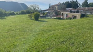 Ein weitläufiges, offenes Grasfeld mit einem Steinhaus, das einen Balkon und einen kleinen Garten mit rosa Blumen besitzt.