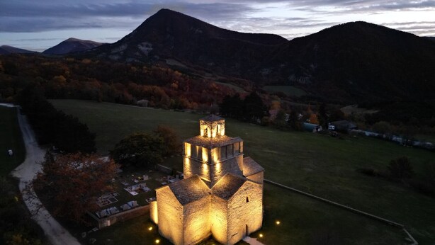 Ein Steinhaus mit einem Turm, umgeben von einer grünen Wiese und Bergen im Hintergrund.